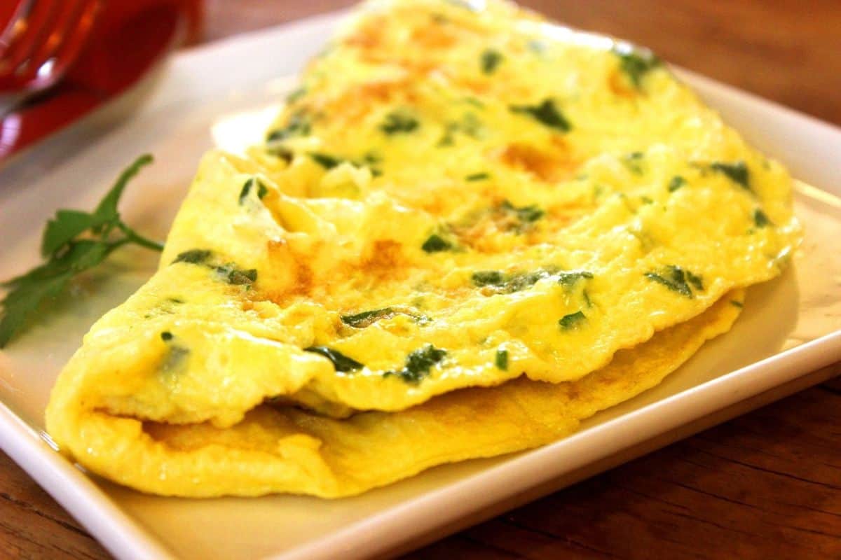 an omelet on a white plate with some chopped herbs.