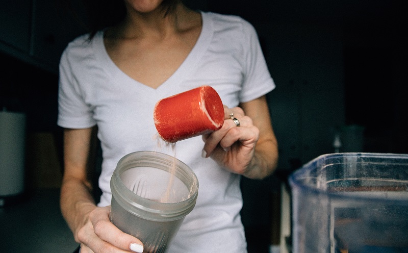 woman in white shirt putting protein powder into blender