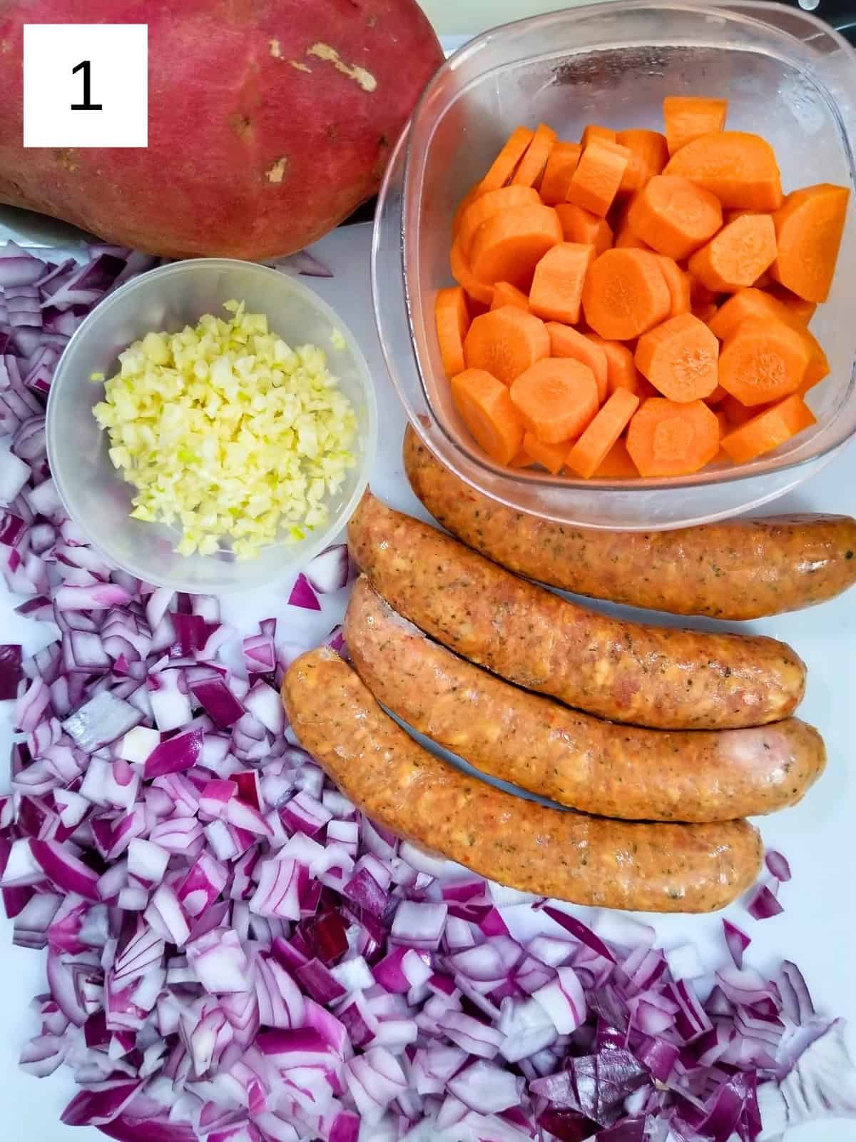 Some of the ingredients for Spanish lentil stew, including sausages, chopped carrots, sweet potato, and minced garlic and onions.