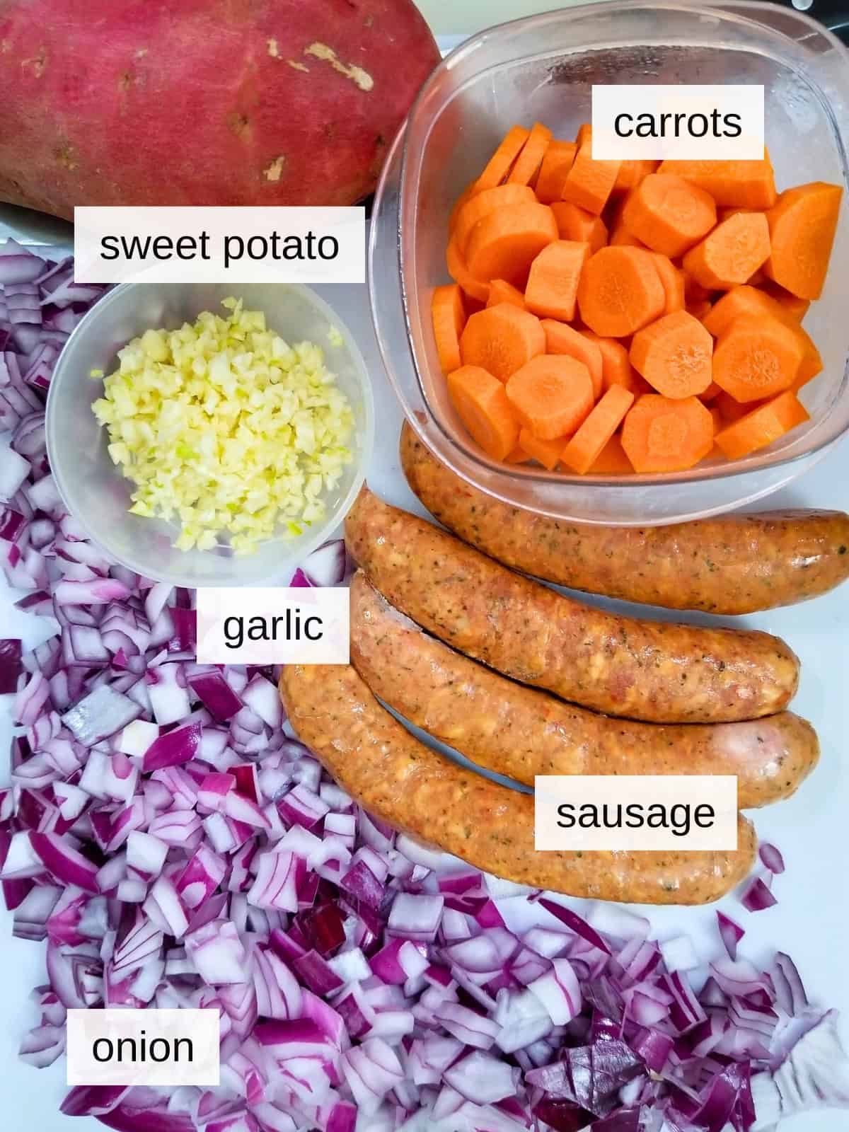 Some of the ingredients for Spanish lentil stew, including sausages, carrots, sweet potato, onions, and garlic.