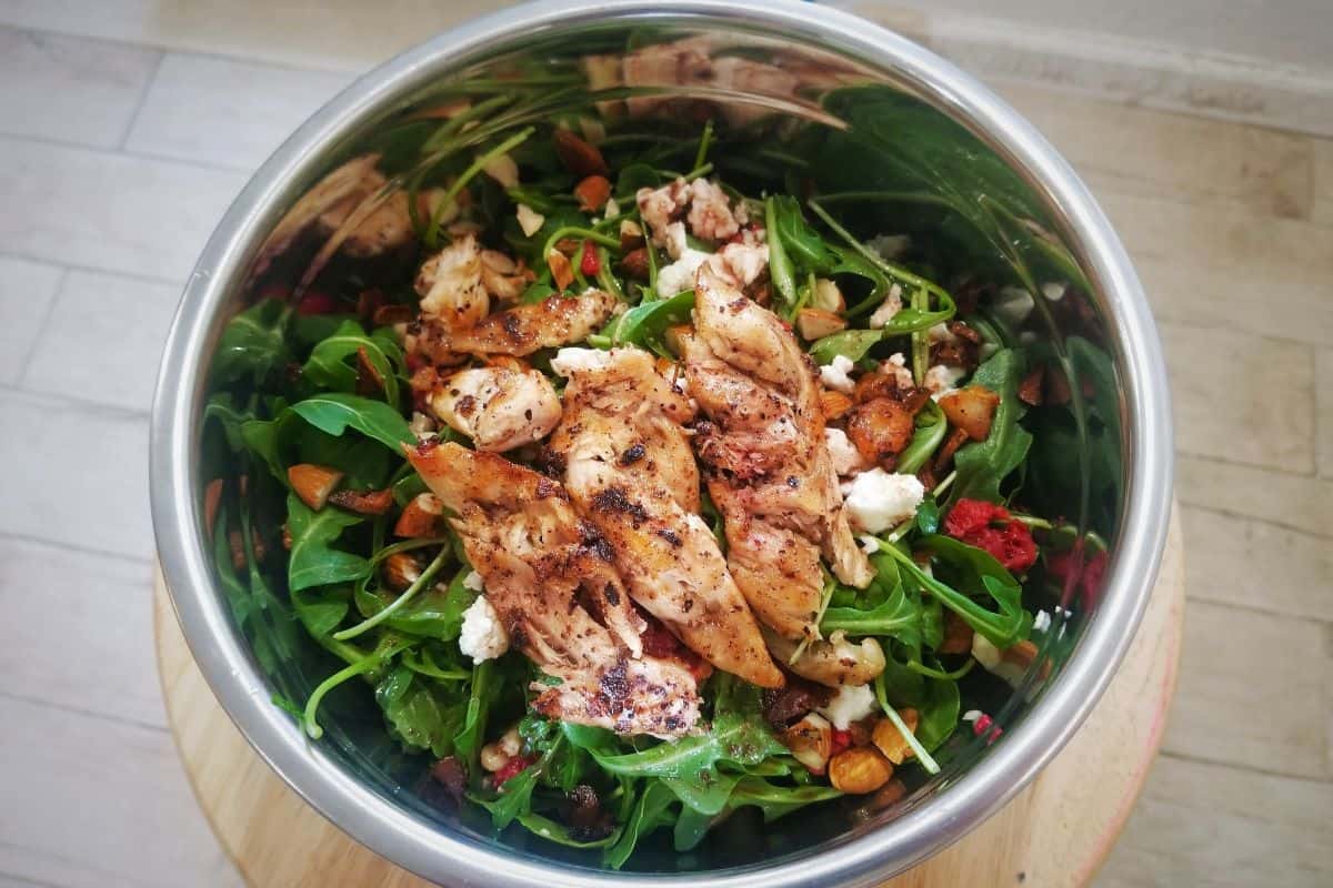 vegetable salad with chicken and pomegranate sumac salad dressing in a mixing bowl.