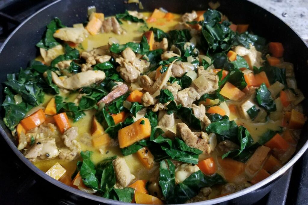 cooked chicken curry topped with kale in a pot.
