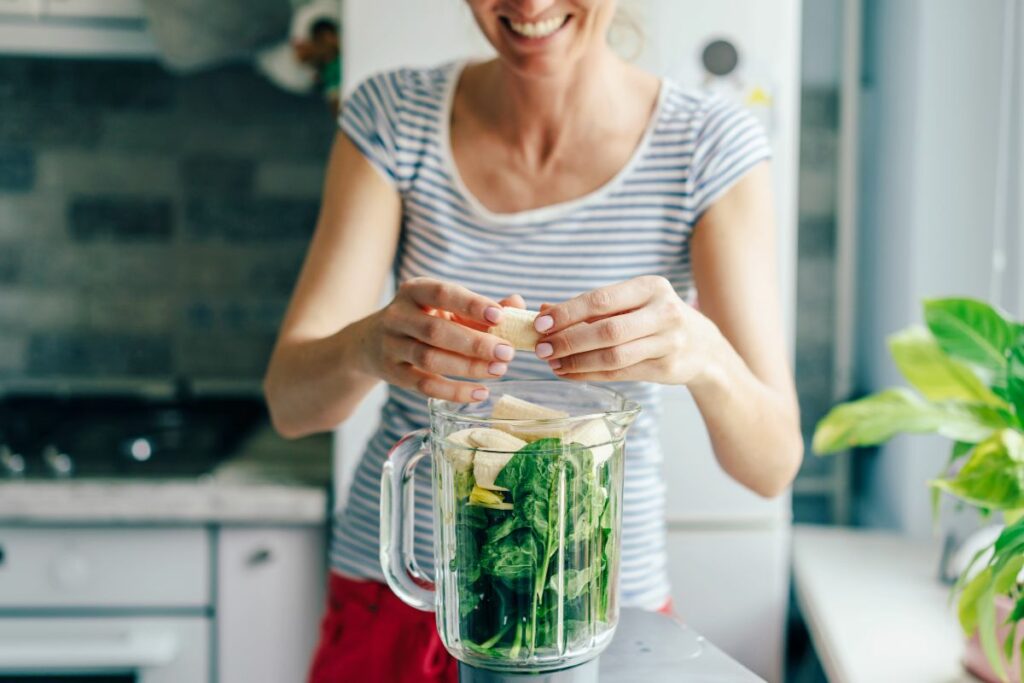 a person making a green smoothie using a blender.