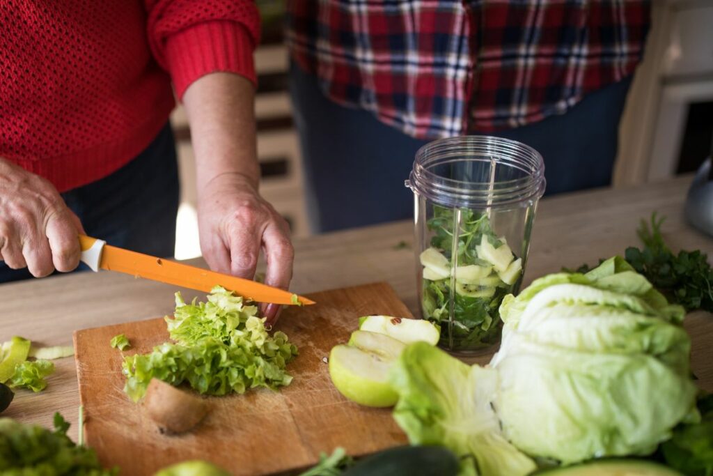 person cutting vegetables for her smoothie white a knife on a cutting board.