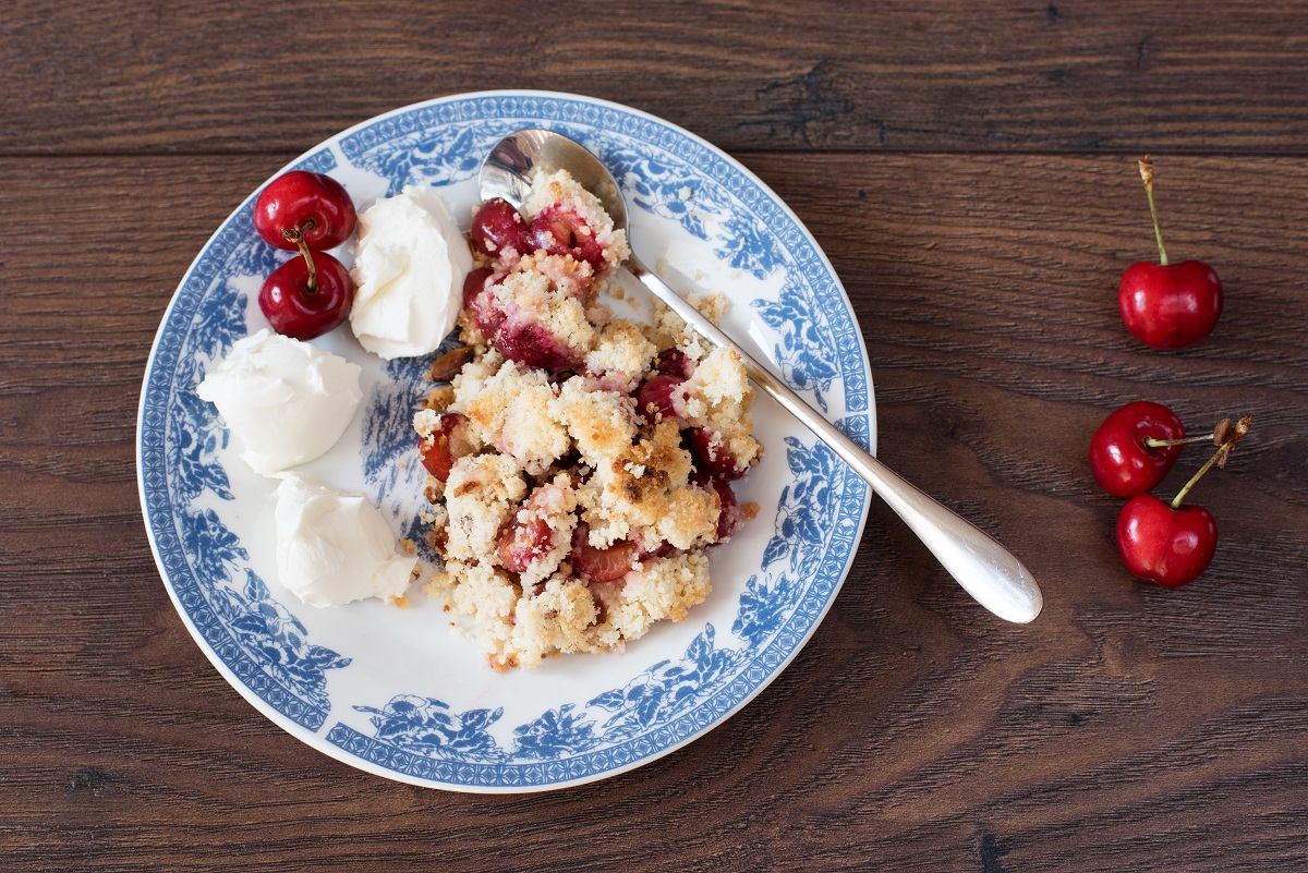 cherry crumble dessert with strawberries and vanilla cream, served on a blue plate. Dark wooden background, top view