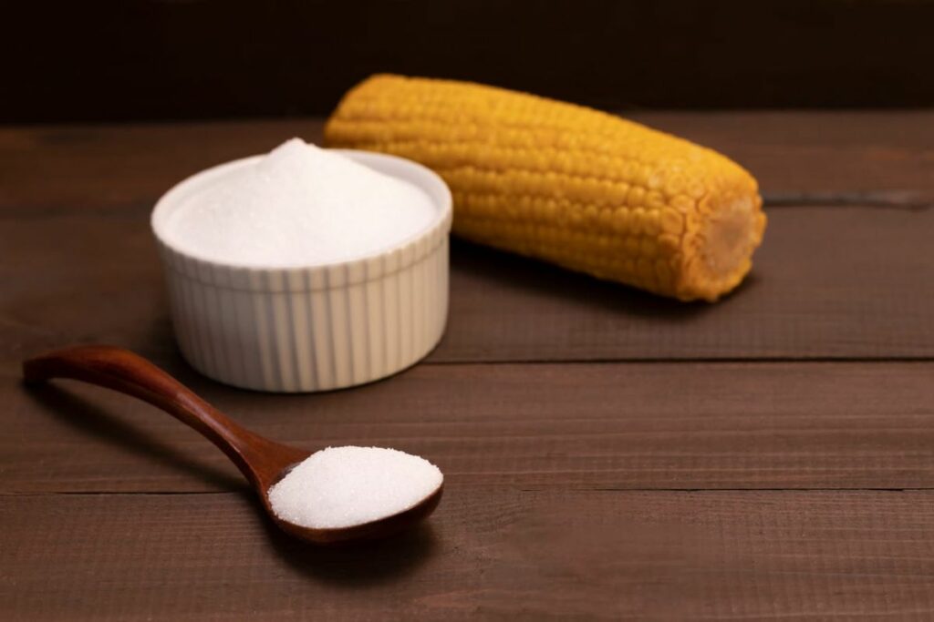 A bowl of allulose next to a whole corn.