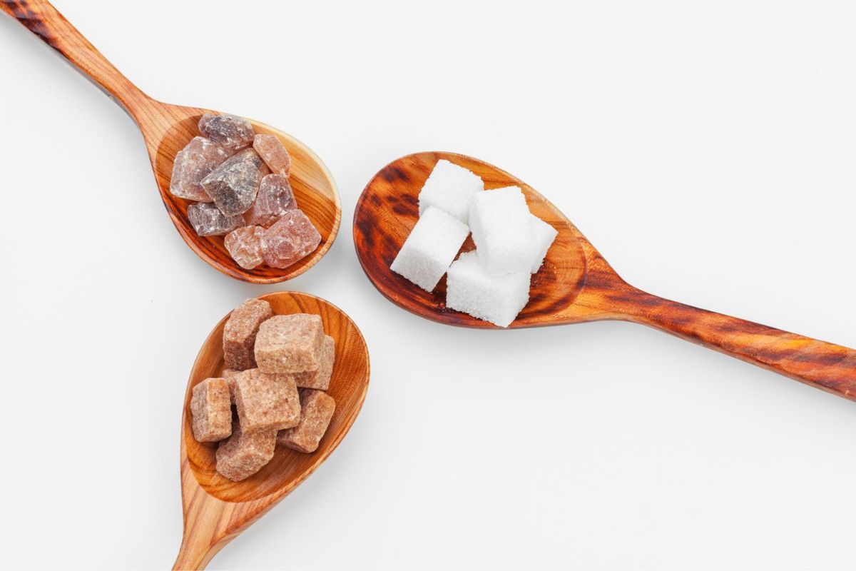 stacked cubes of each brown and white sugar cube, and sugar lumps on wooden spoons on a white background.