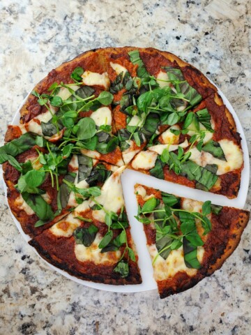 sliced baked pizza with fresh basil on top.