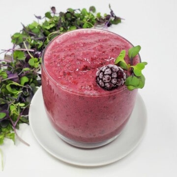a microgreens smoothie in a glass with frozen blackberry and raw microgreens on top.