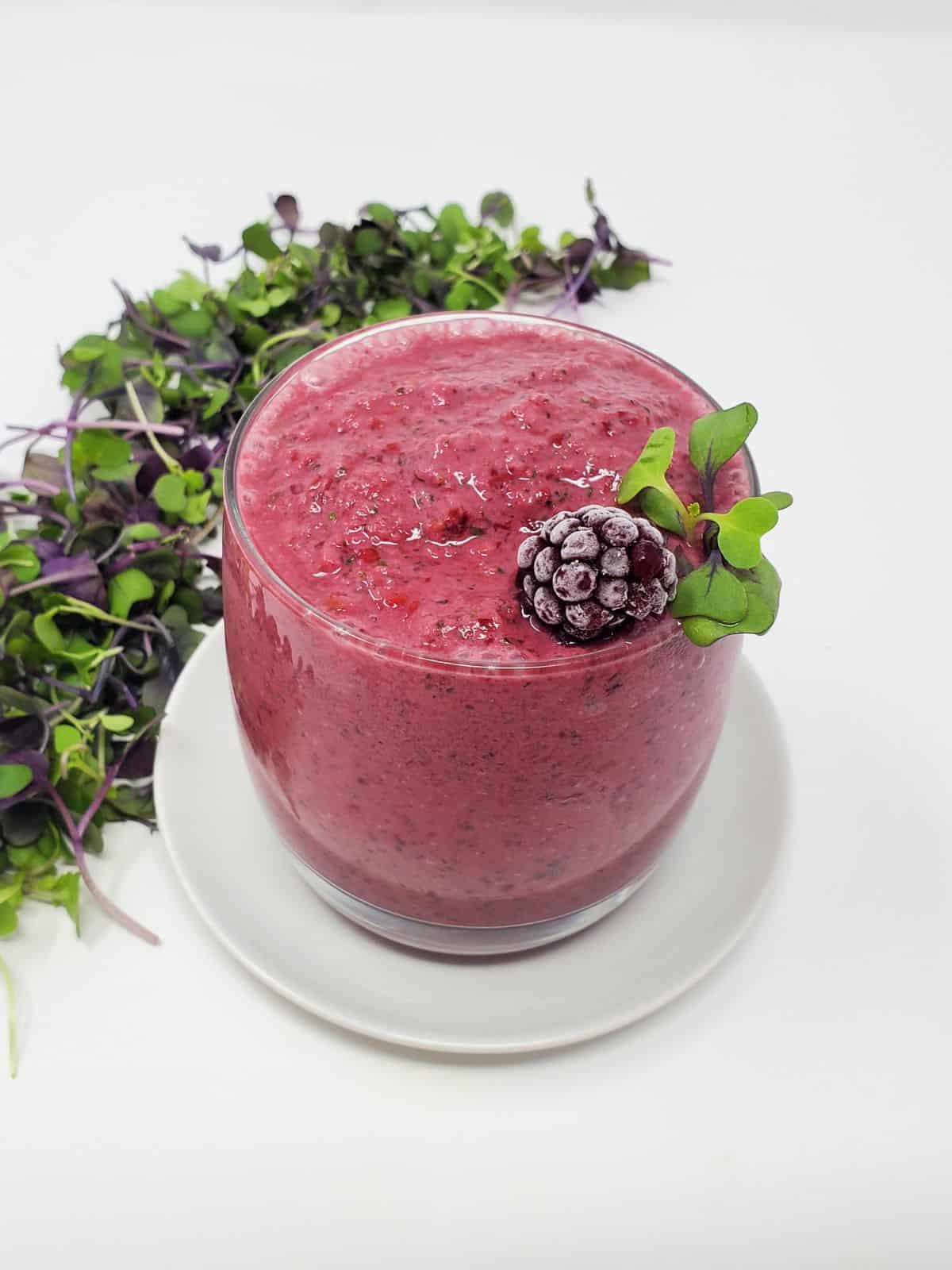 a microgreens smoothie in a glass with frozen blackberry and raw microgreens on top