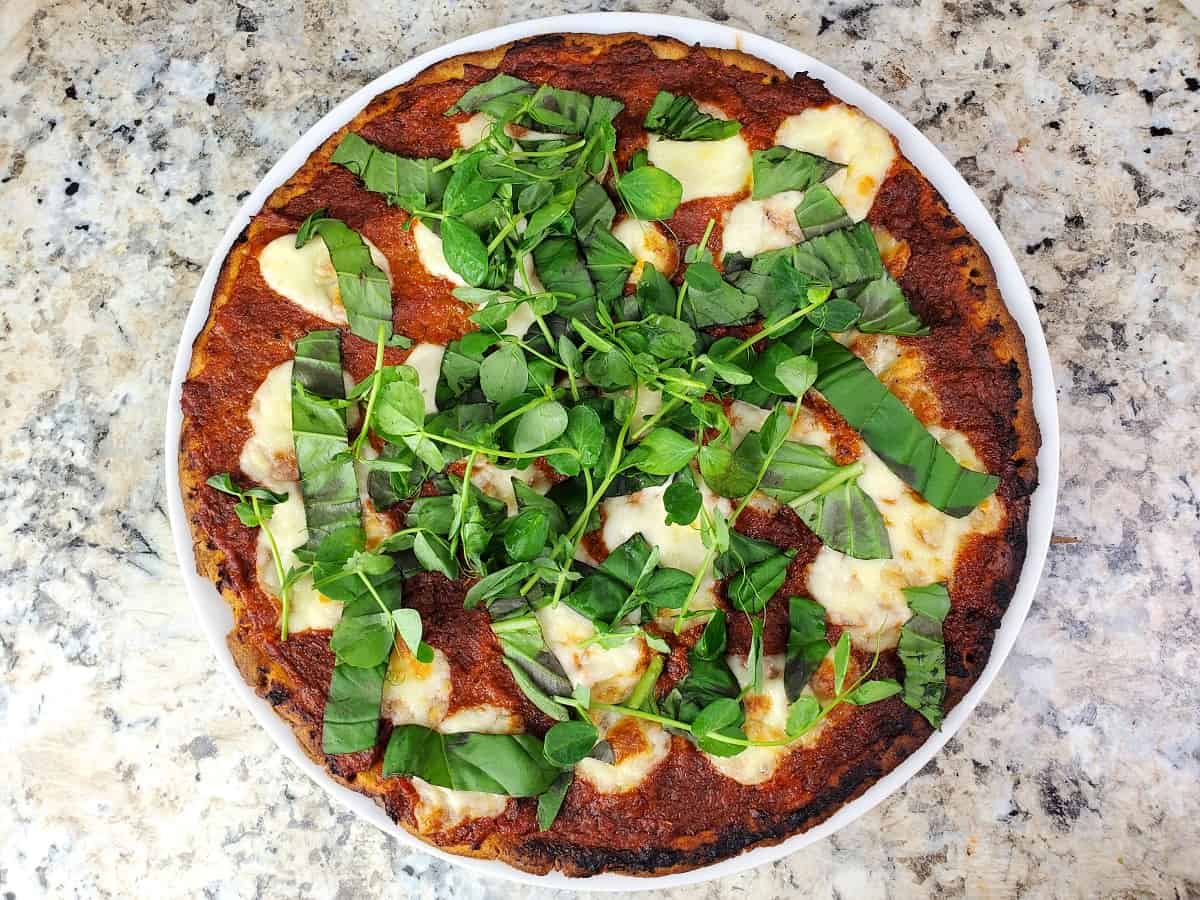 a whole baked pizza topped with fresh basil and microgreens