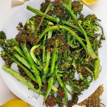 cooked broccolini on a plate surrounded by fresh lemon, garlic, and seasoning.