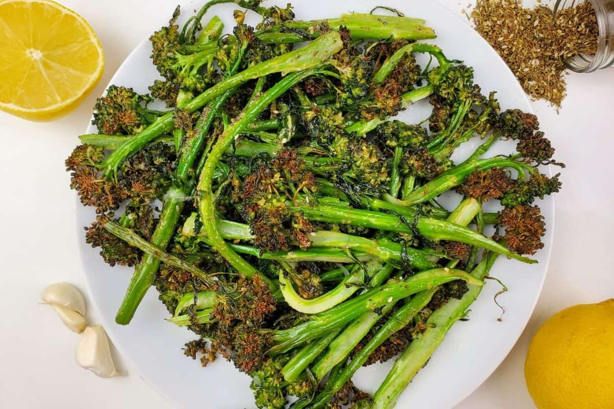 cooked broccolini on a plate surrounded by lemon and garlic.