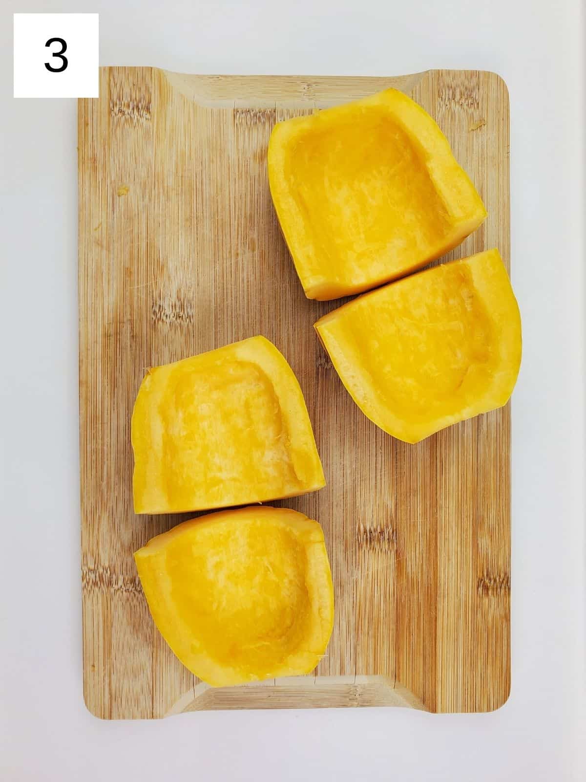 one whole delicata squash, seeds removed and cut into 4 pieces on a wooden cutting board.