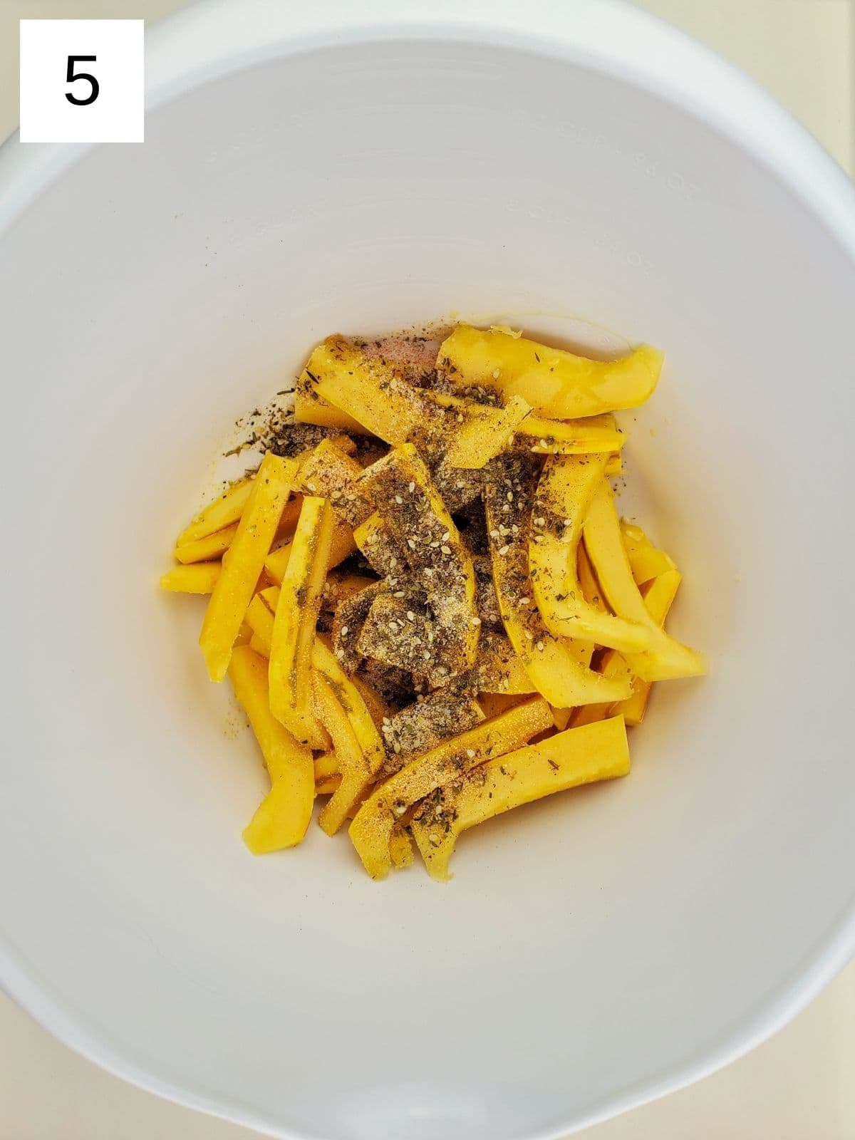 pieces of delicata squash fries in a bowl with seasonings on top.