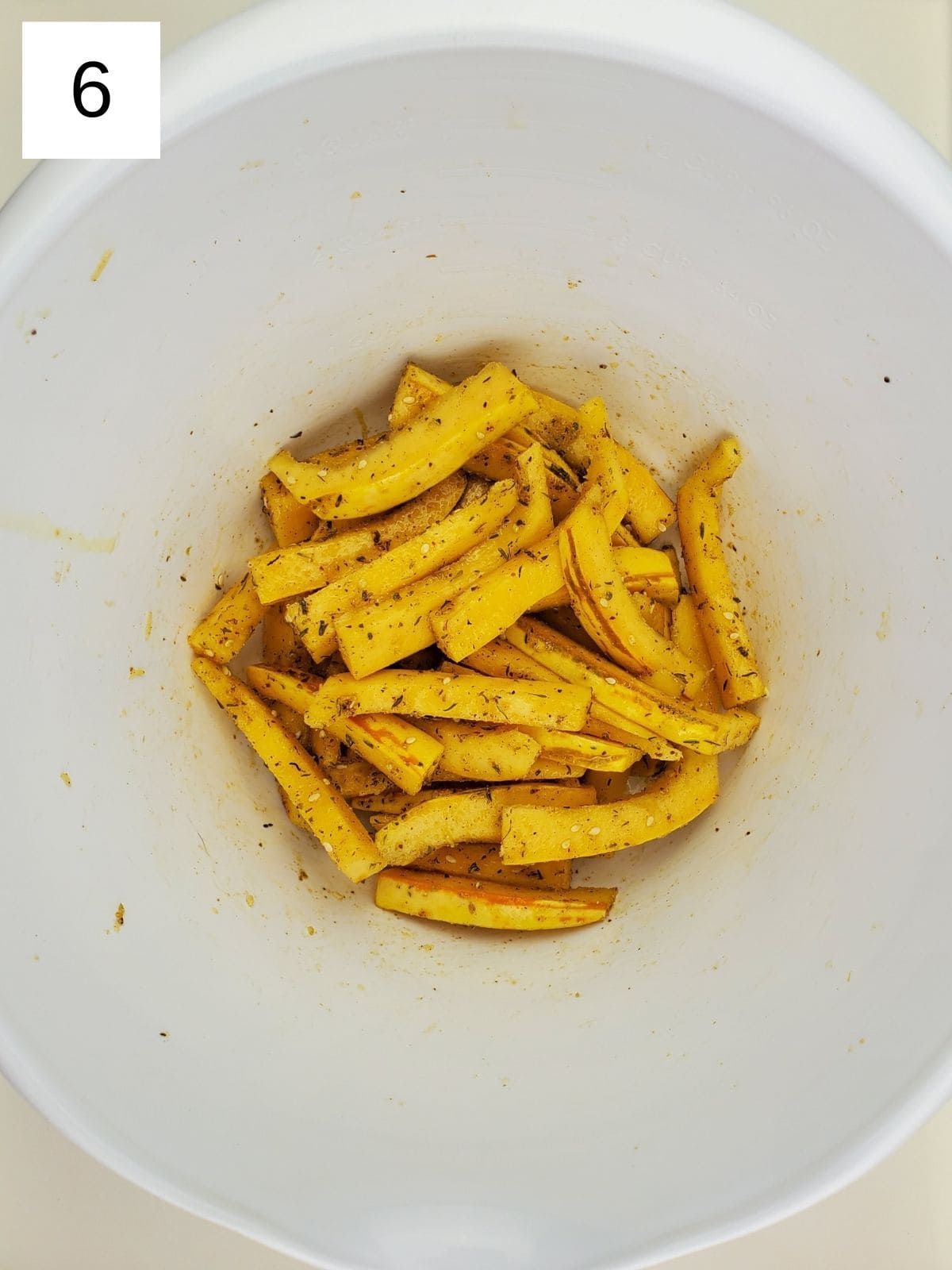 pieces of delicata squash fries tossed in oil & seasonings in a bowl.