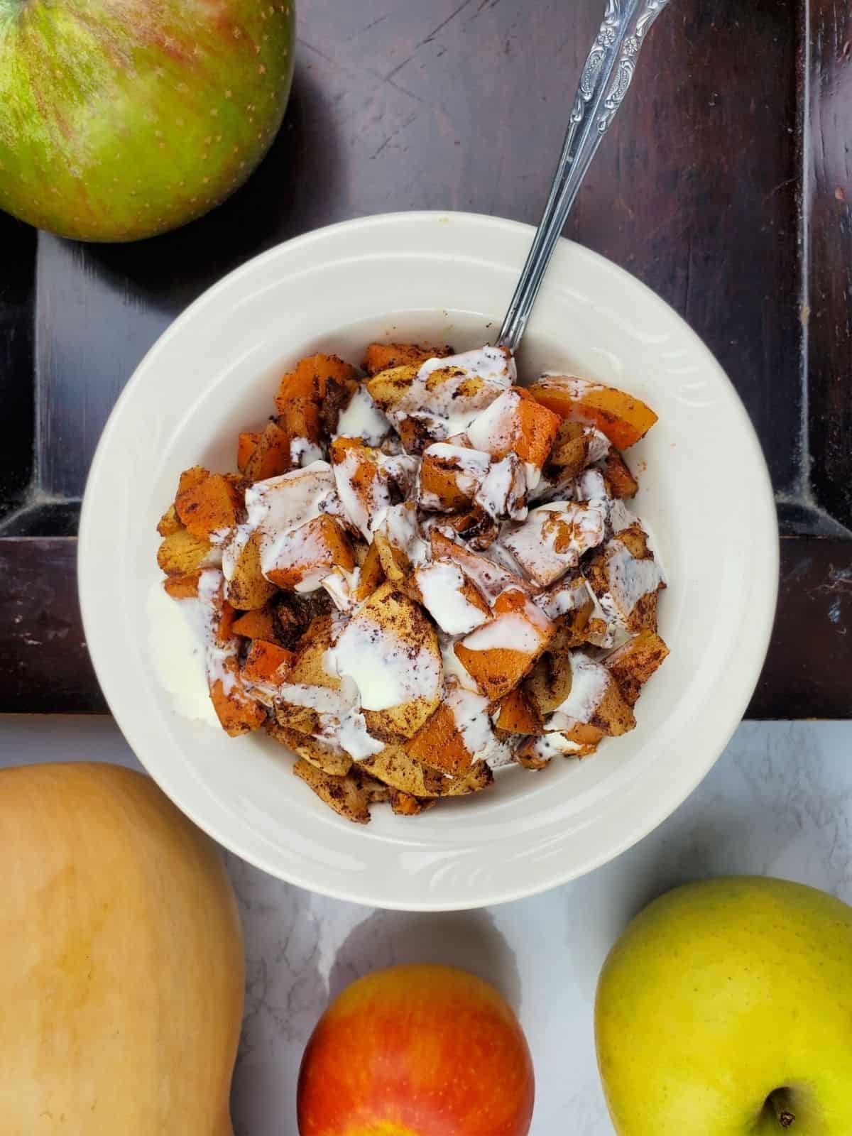 final roasted butternut squash and apples served on a white plate with whipped cream.