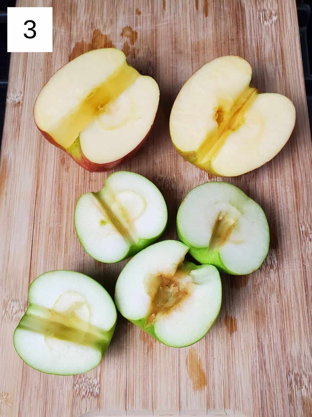 six halves of deseeded apples on a wooden cutting board.