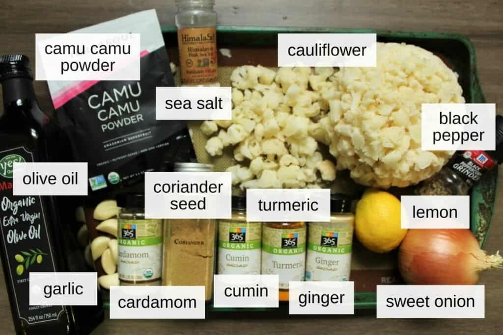 ingredients for baked cauliflower, including camu camu powder, sea salt, fresh cauliflower, olive oil, coriander seed, turmeric, lemon, garlic, cardamom, cumin, ginger, and sweet onion.