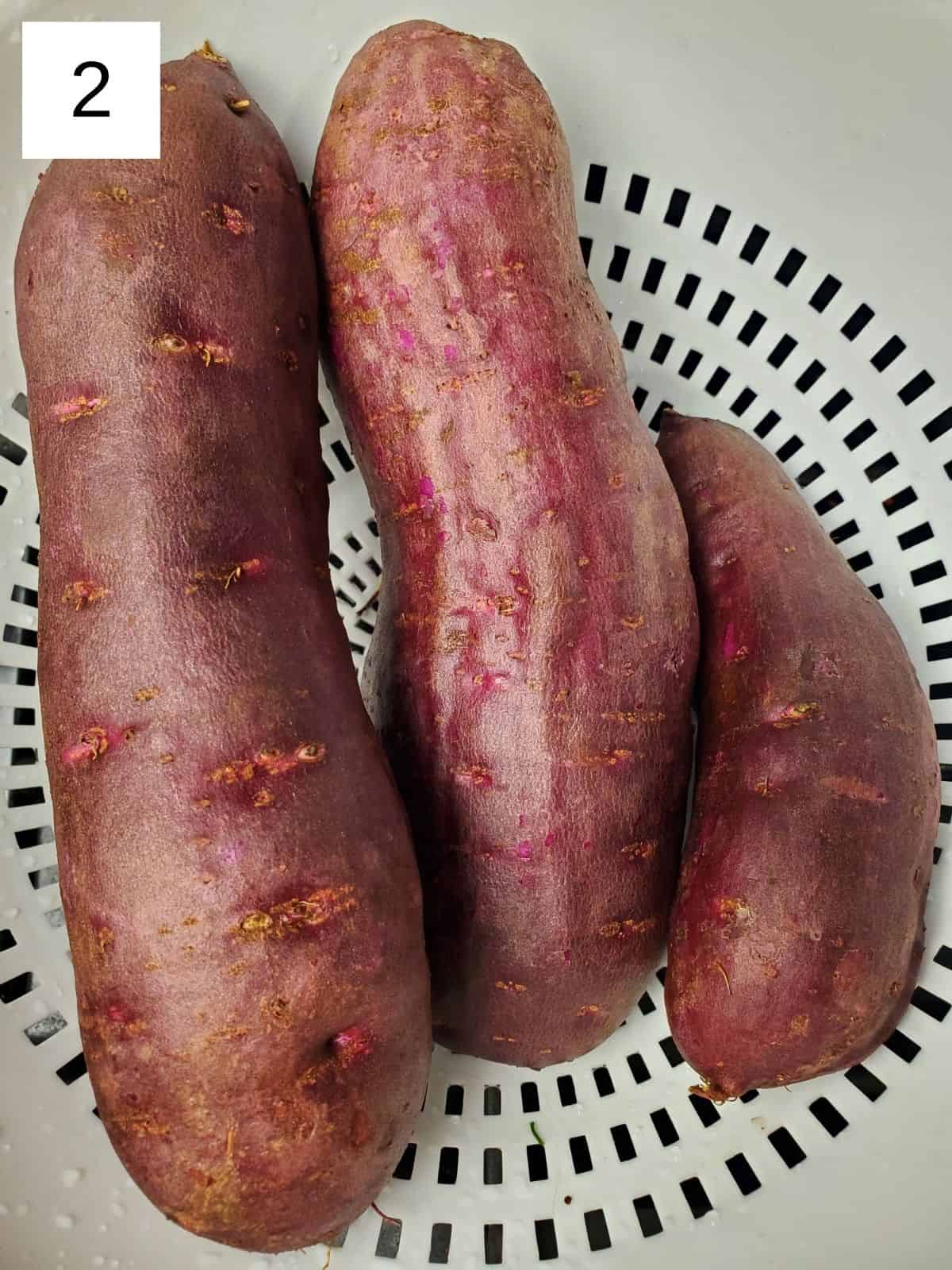 three fresh purple sweet potatoes in a plastic strainer.