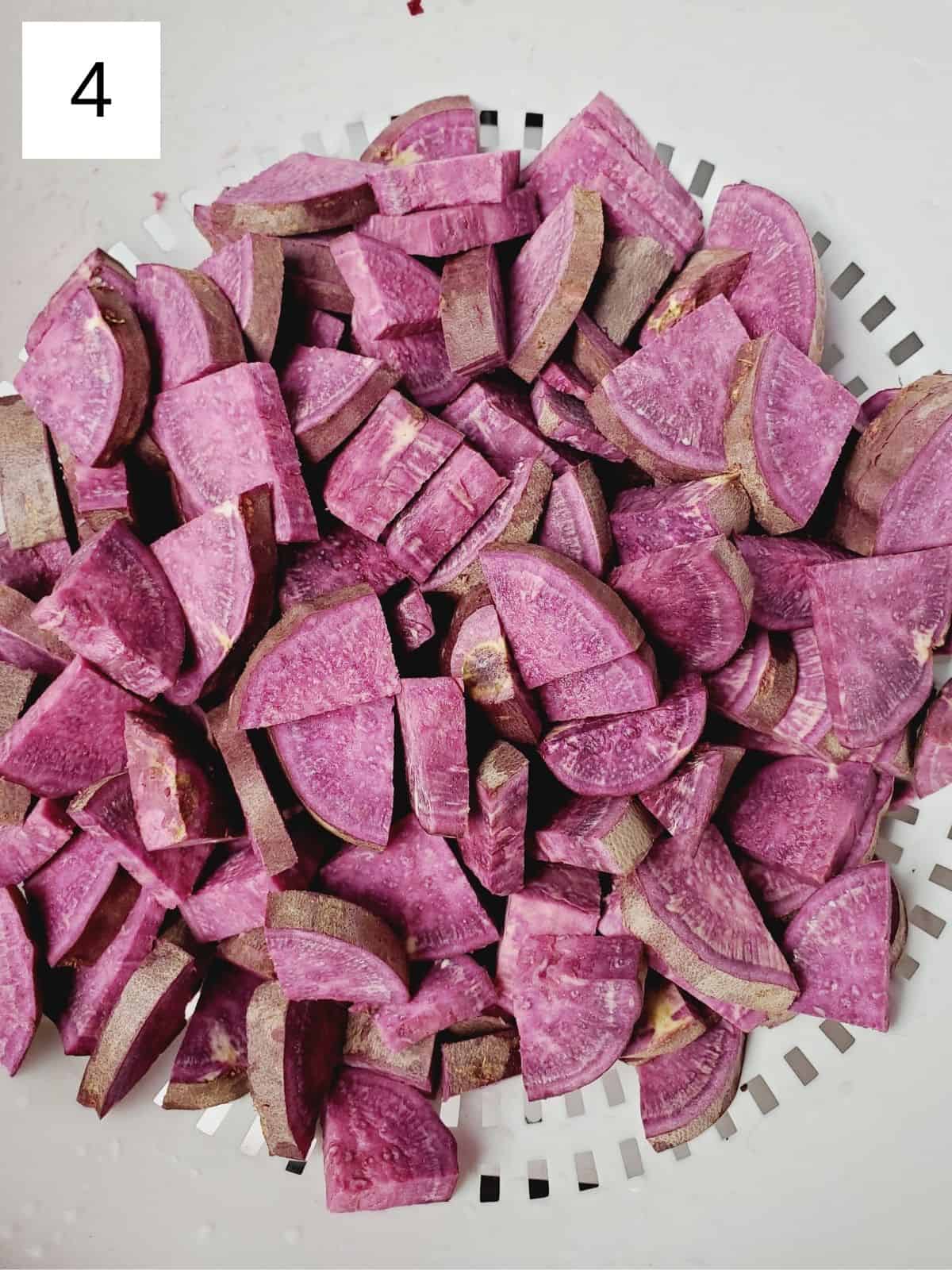 purple sweet potato slices in a white strainer.