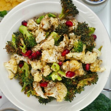 cooked seasoned broccoli and cauliflower, topped with pomegranate seeds, on a white plate.