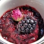 rose blackberry jam in a glass jar with fresh blackberry and rose on top.