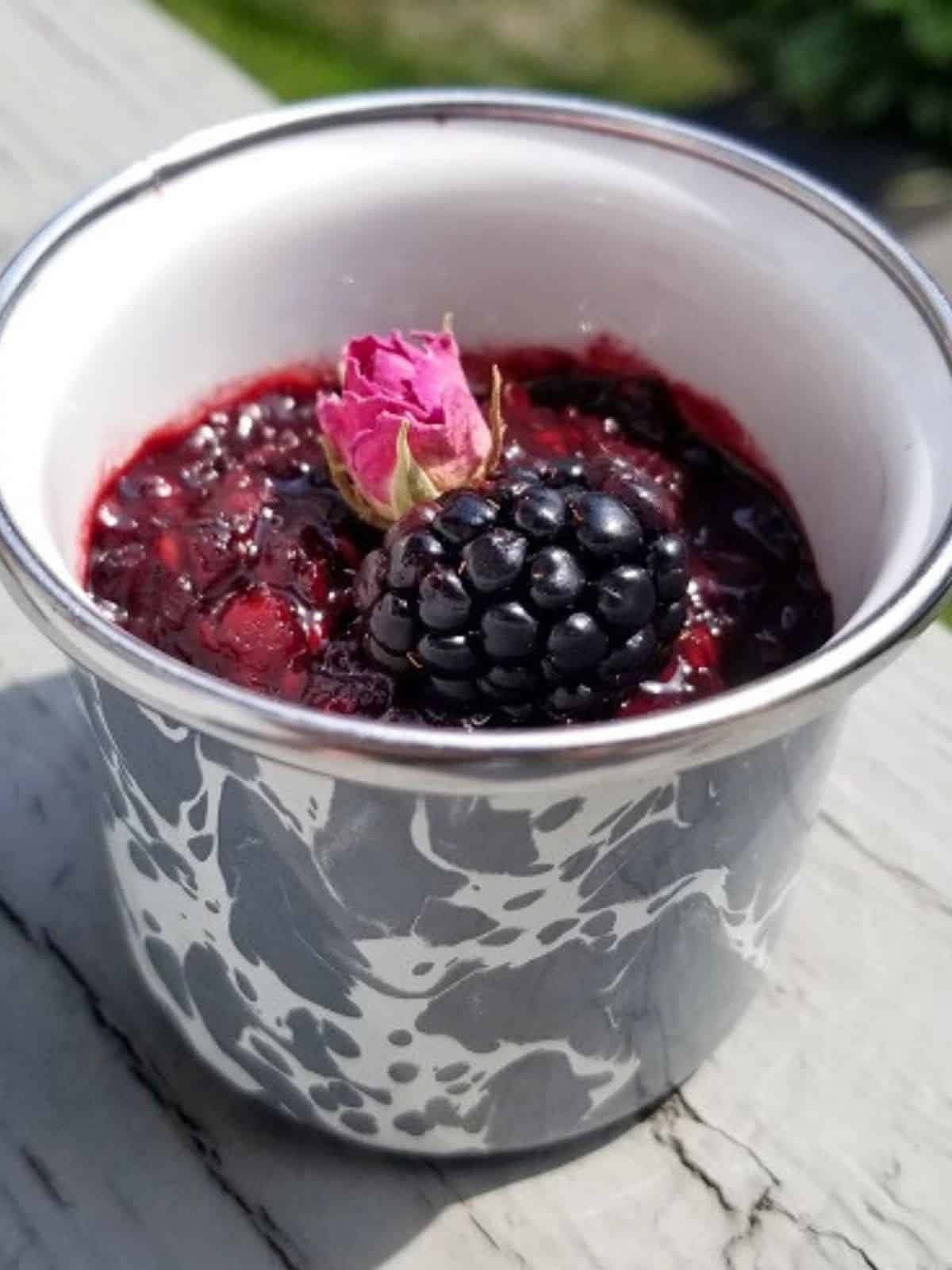 rose blackberry jam in a glass jar with fresh blackberry and rose on top.