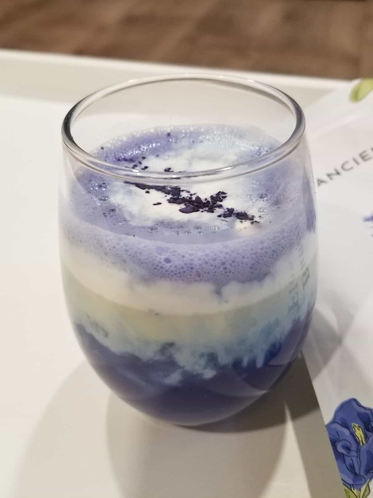 butterfly pea tea latte in a clear glass, topped with whipped cream.