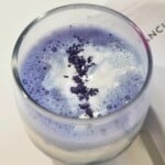 butterfly pea tea latte in a clear glass, topped with whipped cream.