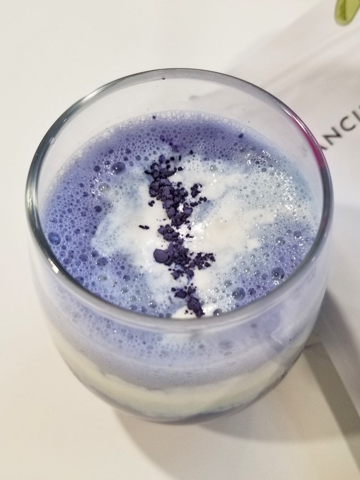 butterfly pea tea latte in a clear glass, topped with whipped cream.