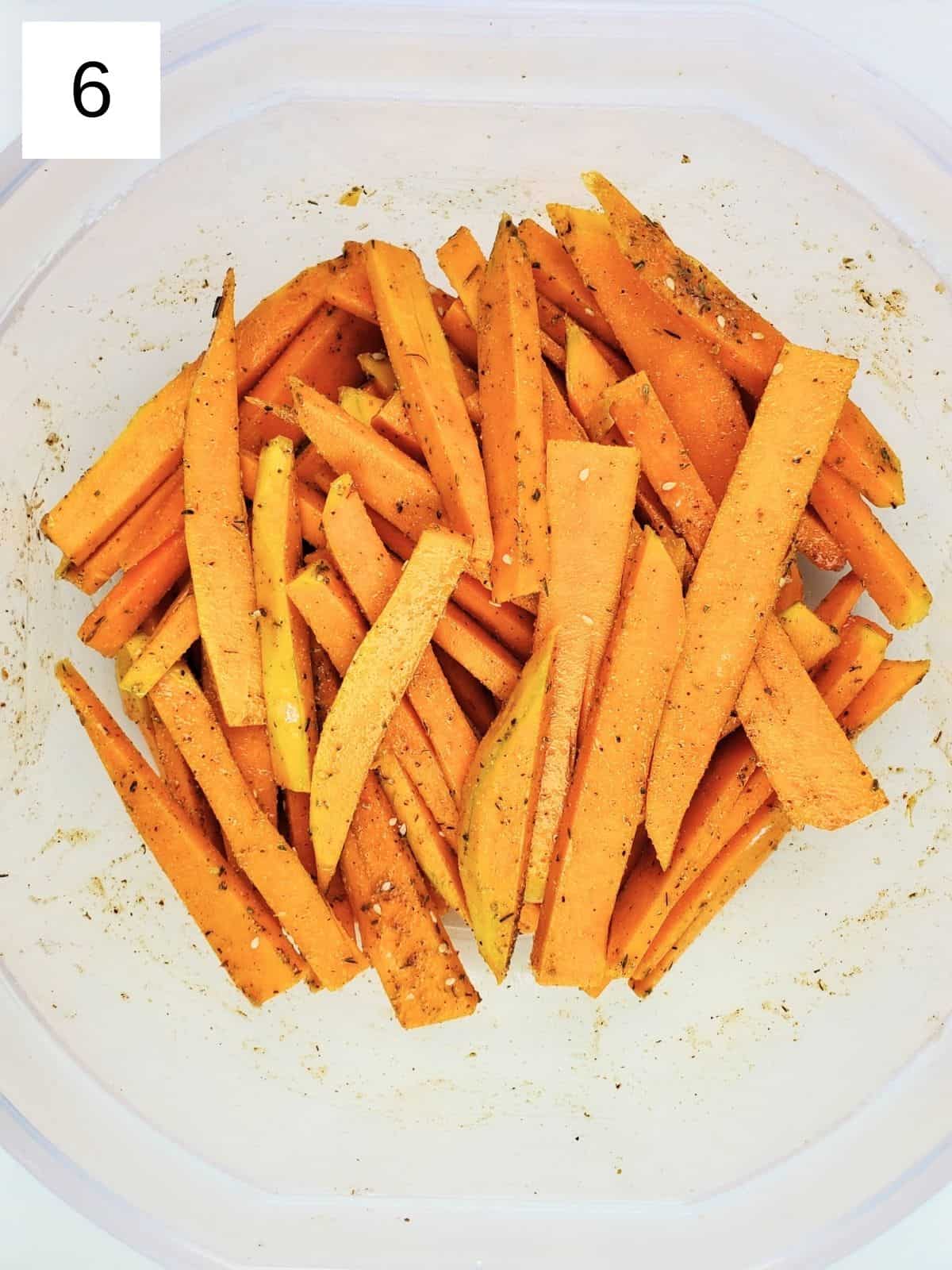 butternut squash slices, coated with seasonings, in a bowl.
