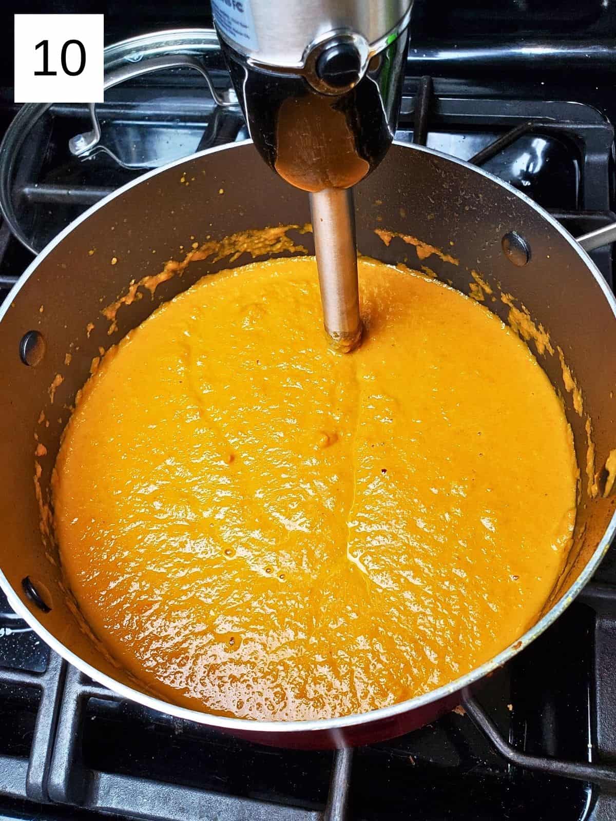 blending the carrot ginger soup mixture using an immersion blender in a pot.