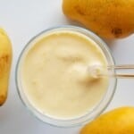 creamy mango smoothie in a glass with three fresh mangoes.
