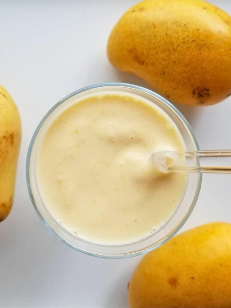creamy mango smoothie in a glass with three fresh mangoes.