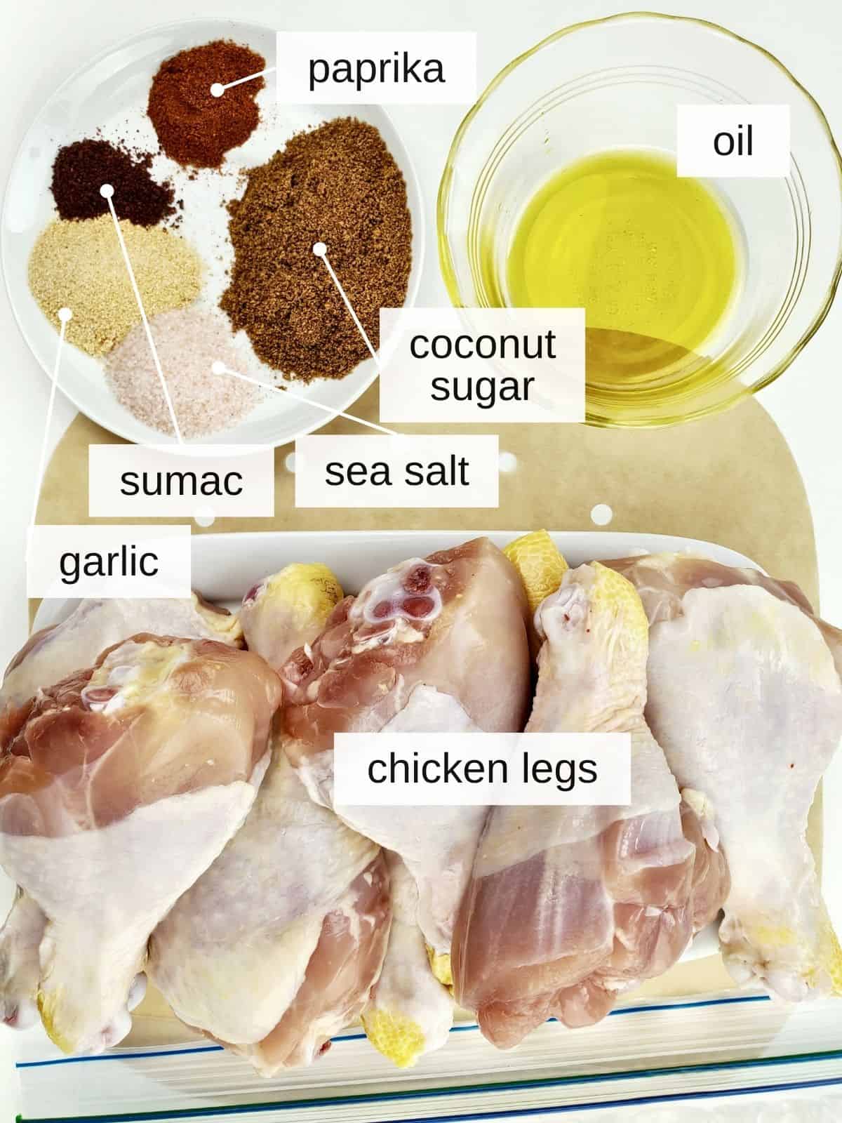 ingredients for air fryer chicken legs, including oil, garlic, sumac, sea salt, coconut sugar, paprika, and chicken legs.