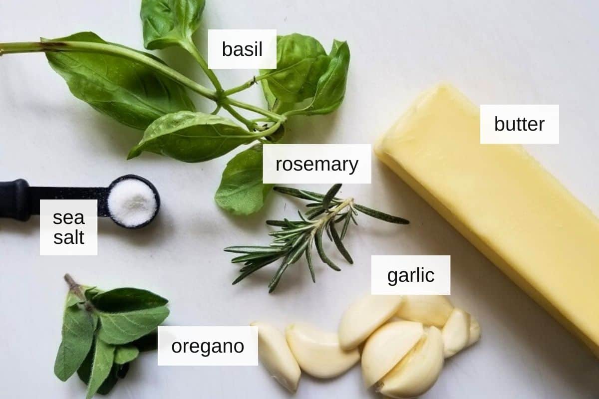 Ingredients for garlic herb compound butter, including oregano, basil leaves, rosemary, garlic, butter, and sea salt.