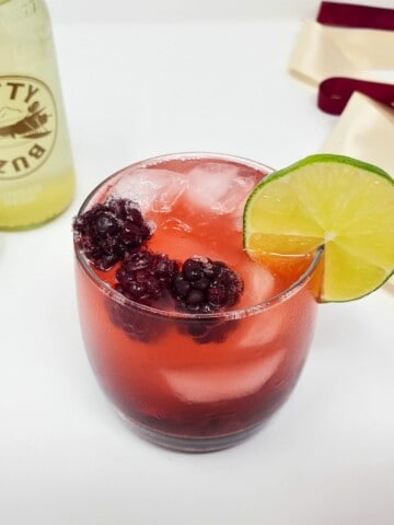 blackberry ginger beer mocktail, topped with frozen blackberries and a slice of lime in a drinking glass.