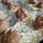 baked even-sized lamb meatballs in a foil-wrapped baking tray.