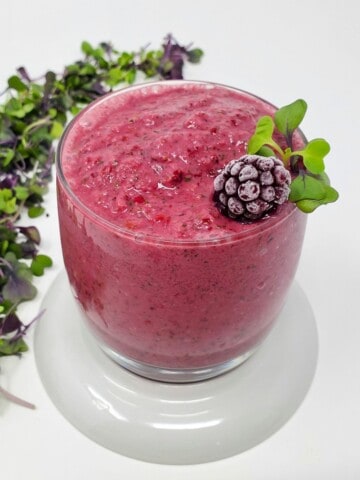 a microgreens smoothie in a glass with frozen blackberry and raw microgreens on top.