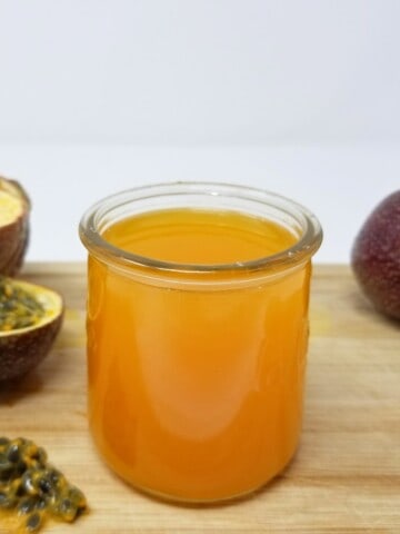 passion fruit syrup in a glass container and some fresh passion fruits on a wooden cutting board.