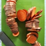 equally sliced sweet potatoes on a green cutting board.