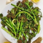 cooked broccolini on a plate surrounded by lemon and garlic.