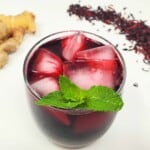 roselle tea in a drinking glass served with ice and topped with basil leaves.