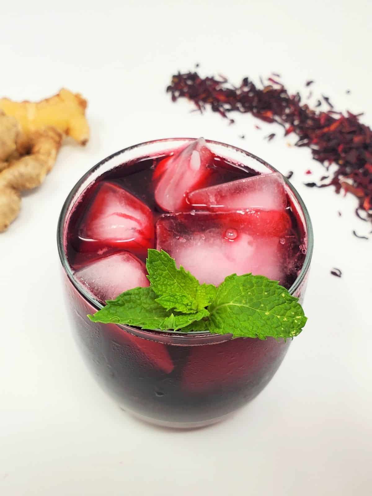roselle tea in a drinking glass served with ice and topped with basil leaves.