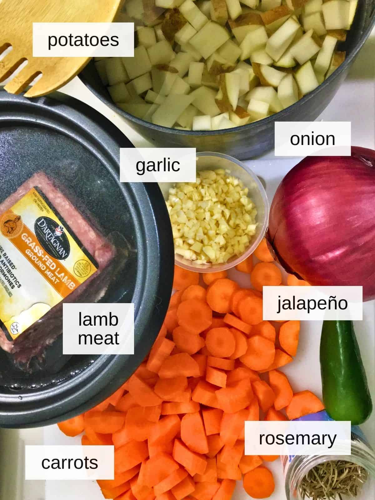 rosemary garlic lamb skillet ingredients, including potatoes, garlic, onion, jalapeño, lamb meat, rosemary, and carrots.