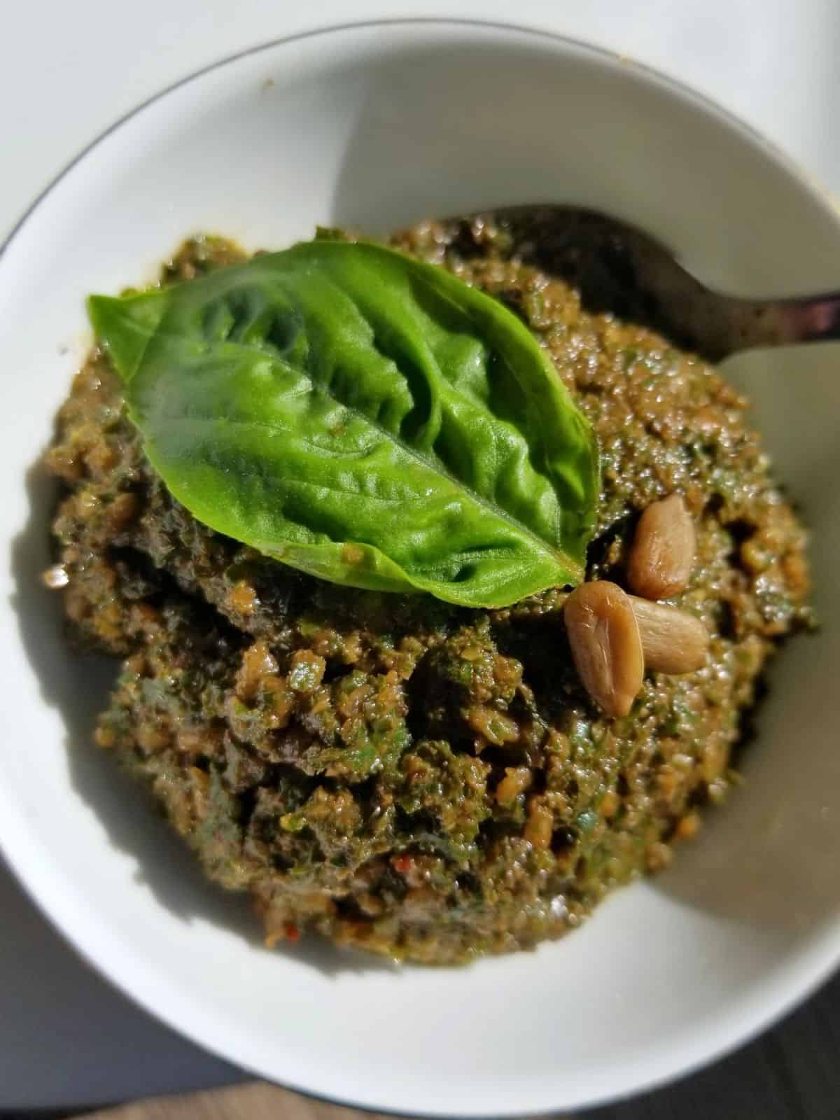 sunflower seed pesto in a glass bowl topped with sunflower seeds and fresh basil leaf.