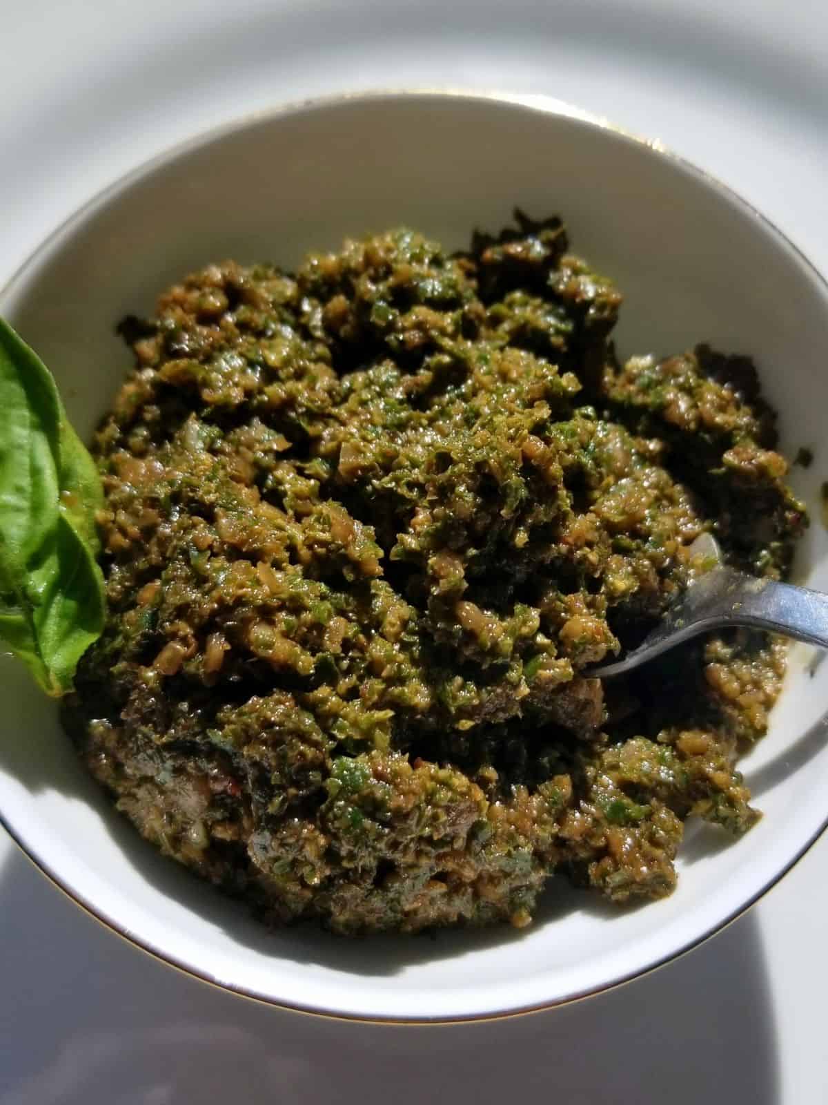 sunflower seed pesto in a glass bowl topped with fresh basil leaf.