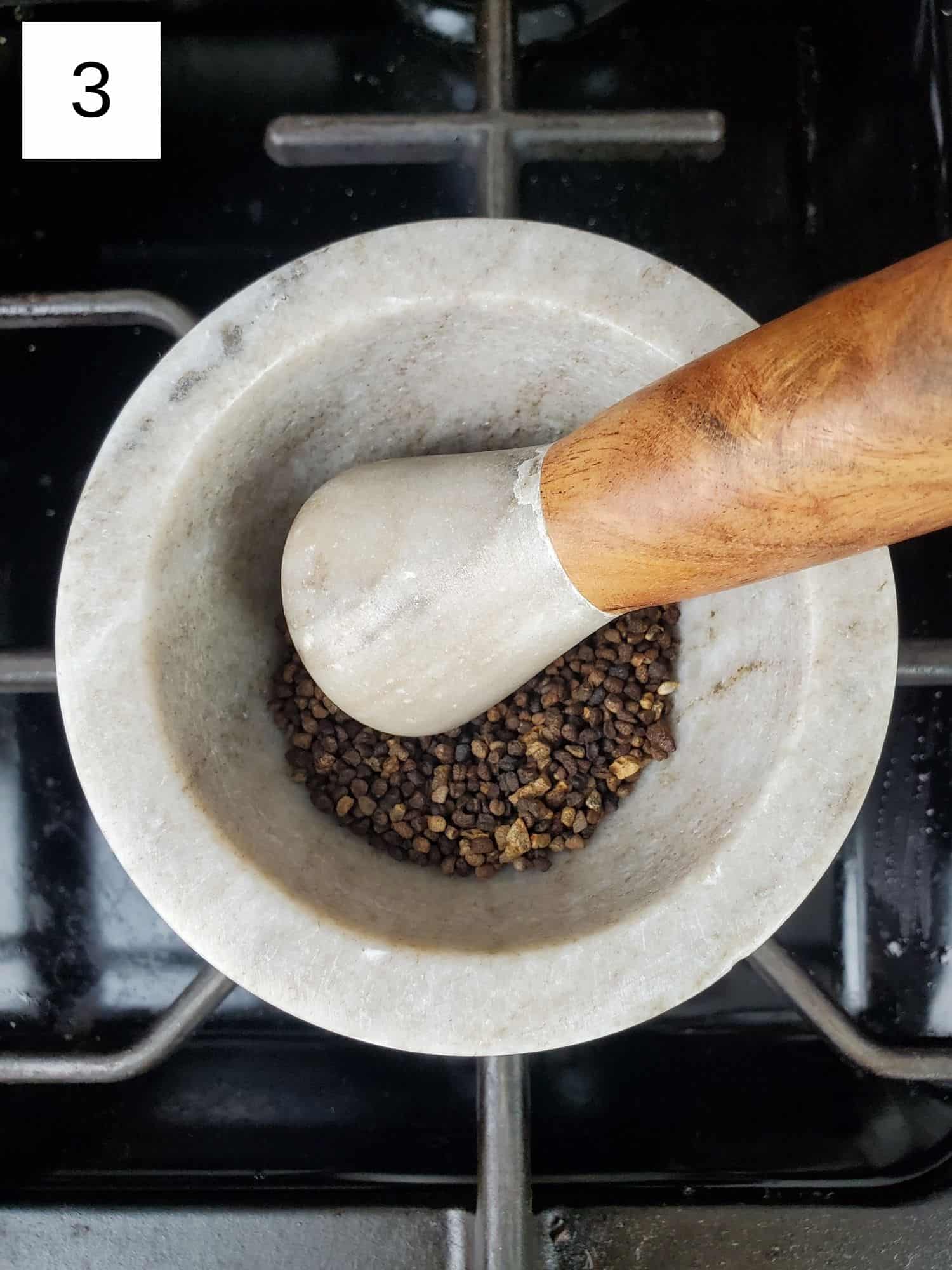 grinding the toasted cardamom seeds using a mortar and pestle.