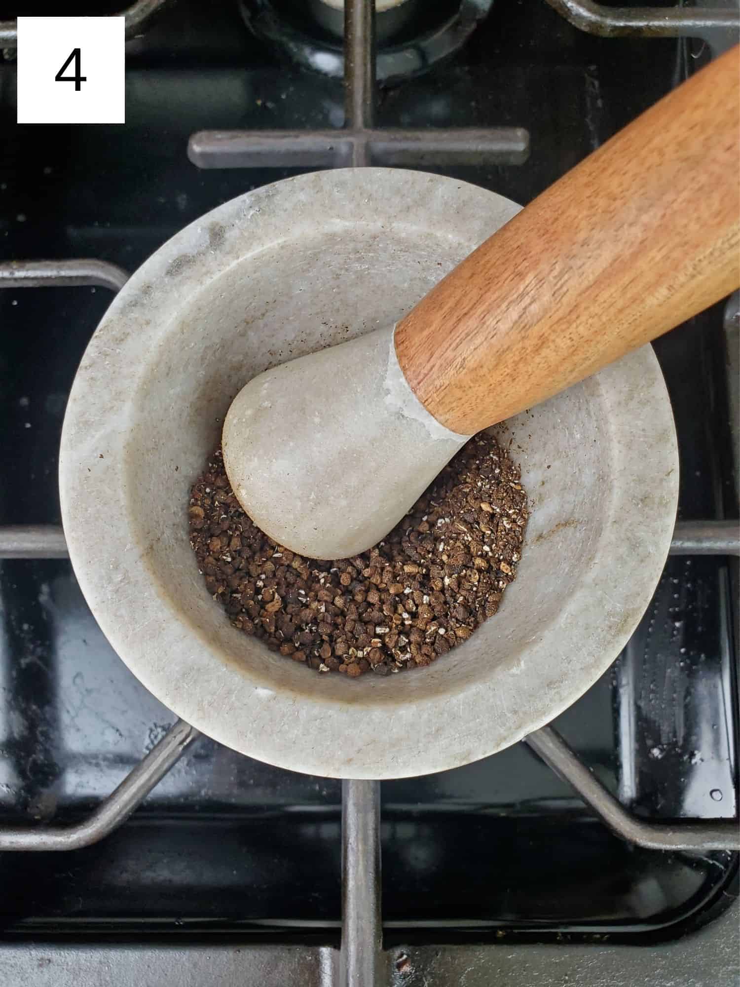 grinding the toasted cardamom seeds using a mortar and pestle.